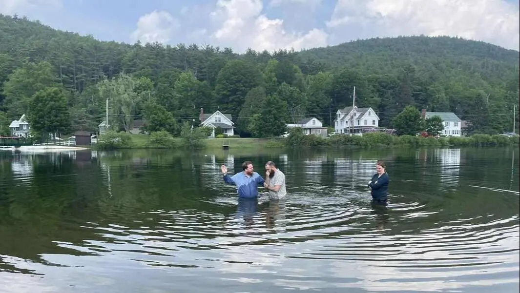 A baptism in Brant Lake with the church family watching from the shore